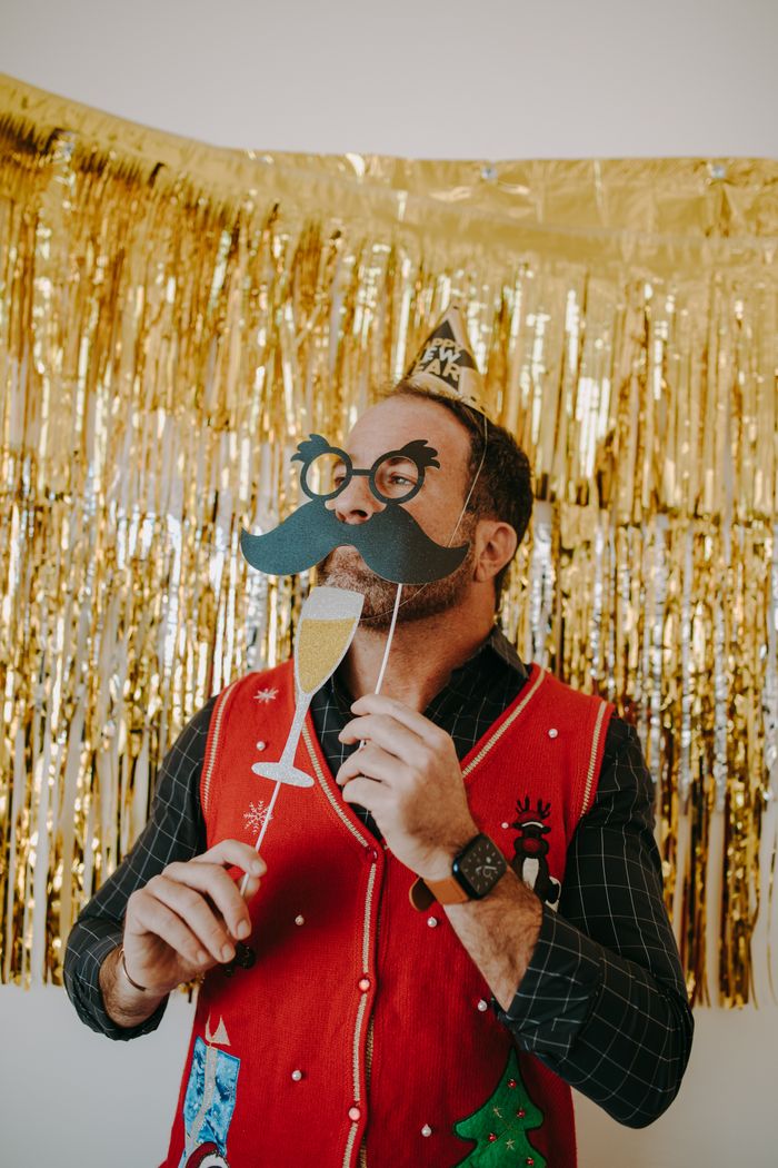 Man in festive attire holding paper props at a celebration with gold decor.